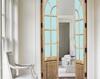 Puede incluir: Un par de puertas francesas de madera con paneles de vidrio esmerilado y parte superior arqueada. Las puertas están abiertas y revelan una habitación con una alfombra blanca y un sillón blanco.