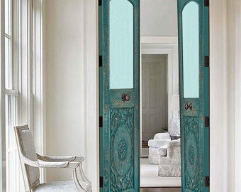 May include: A pair of teal-colored, carved wooden doors with arched glass panels. The doors feature ornate floral and scrollwork designs and are set in a white doorway. The doors are open, revealing a glimpse of a room beyond.