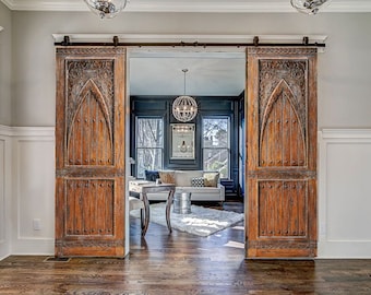 May include: A pair of rustic wooden barn doors with intricate carvings and metal accents, open to reveal a room with a white rug, a couch, and a coffee table.