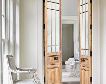 Puede incluir: Un par de puertas dobles de madera con paneles de vidrio y pomos negros. Las puertas están abiertas y revelan una habitación con una alfombra blanca y una silla.
