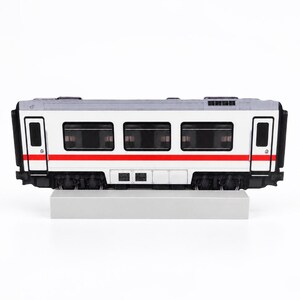 May include: A model train carriage featuring a white exterior with a horizontal red stripe running along the middle. The carriage has black window frames, dark tinted windows, and black undercarriage details, resting on a rectangular base.