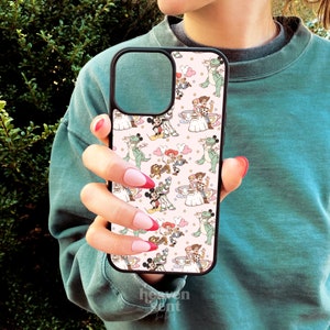 May include: A pink and white phone case with a repeating pattern of cartoon characters from Disney's Toy Story and Mickey Mouse. The characters are in various poses, including standing, sitting, and waving. The case is made of a hard plastic material and has a black border.