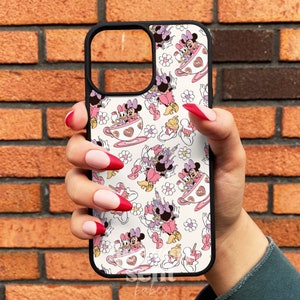 May include: A white phone case with a black border featuring a repeating pattern of Minnie Mouse and Daisy Duck in teacups. The characters are pink and white with black outlines. The background is white with pink flowers and cupcakes.