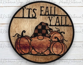 May include: A round wooden sign with the text "It's Fall Y'all" in black lettering. A gnome with a black and white checkered hat is sitting in front of three pumpkins.