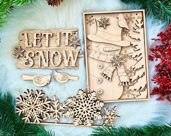Könnte beinhalten: Holzbastelset mit einem Schneemann, zwei Vögeln, Schneeflocken und einem Schild mit der Aufschrift "Let it Snow".