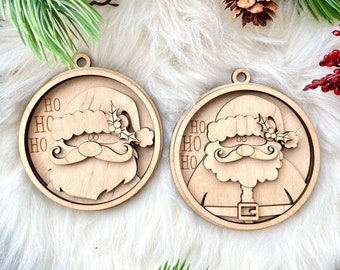 Puede incluir: Dos adornos navideños de madera con un Papá Noel de dibujos animados con barba blanca y gorro rojo. Los adornos son redondos y tienen las palabras "HO HO HO" escritas en ellos.