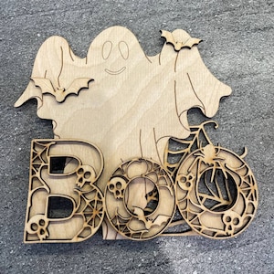 May include: Wooden cutout of a ghost with bats and the word "BOO" in a spooky font with spiderwebs and skulls.