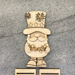 May include: Wooden Uncle Sam figure with a top hat, fireworks, and stars. The word "America" is displayed on the figure. Includes two rectangular wooden stands. Ideal for patriotic decor.