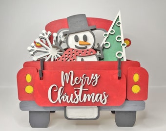 May include: A red wooden truck with a snowman, a Christmas tree, and a snowflake in the back. The truck has a white sign that says "Merry Christmas".