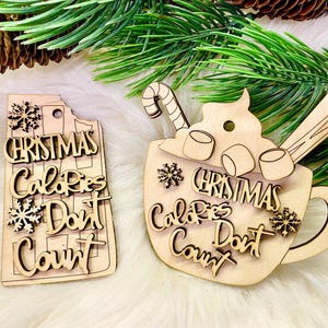 Pode incluir: Dois enfeites de Natal de madeira com o texto "Christmas Calories Don't Count". Um enfeite tem a forma de uma caneca de chocolate quente com marshmallows e um bastão de caramelo. O outro enfeite é um retângulo.