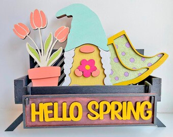 May include: A wooden gnome figurine sitting on a black wooden bench with a flower pot and tulips. The bench has a sign that says "HELLO SPRING".