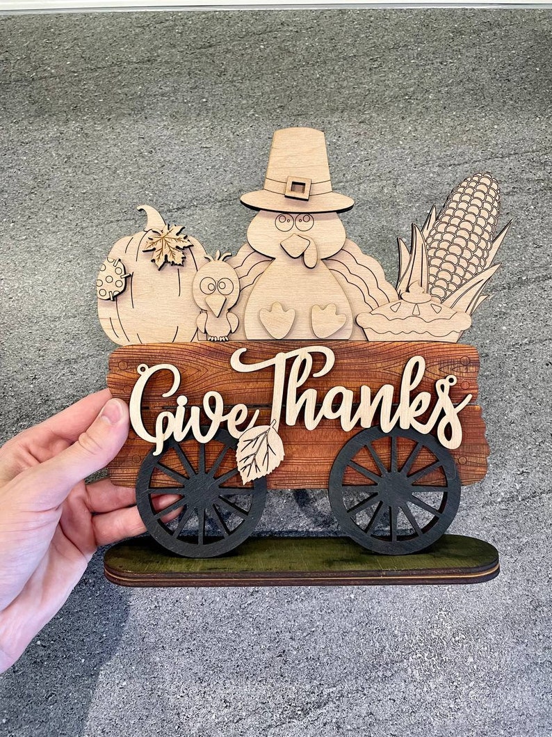 K&ouml;nnte beinhalten: Ein h&ouml;lzernes Thanksgiving-Schild mit einem Truthahn, einem K&uuml;rbis, Mais und einem Wagen mit den Worten "Give Thanks".