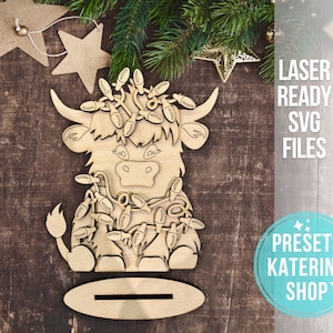 May include: A wooden cutout of a Highland cow with a festive garland of lights around its neck. The cutout is designed for laser cutting and is part of a set of SVG files.