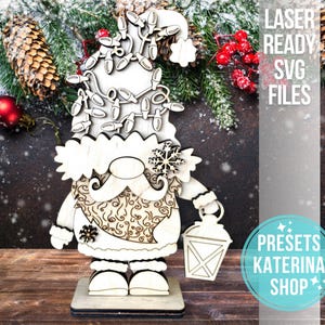 May include: Wooden Christmas gnome with a hat decorated with fairy lights, a snowflake, and a lantern. The gnome features a patterned belly and stands on a wooden base. The text "LASER READY SVG FILES" is visible.