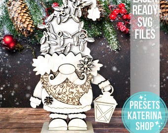 May include: Wooden Christmas gnome with a hat adorned with string lights, a snowflake, and a lantern. The gnome has a patterned belly and is standing on a wooden base. The text "LASER READY SVG FILES" is visible.