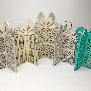 Könnte beinhalten: Fünf dekorative Geschenkkisten aus Holz, jede mit einem anderen Design. Die Kisten sind in Weiß-, Creme- und Türkistönen gehalten.