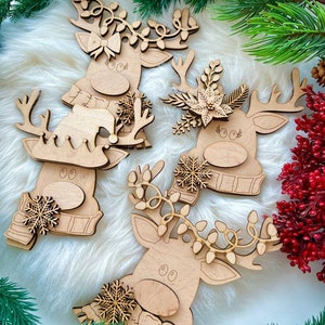 May include: Four wooden reindeer ornaments with different decorations. Each reindeer has a brown wooden body with a white face and black eyes. The reindeer are decorated with snowflakes, greenery, and lights.