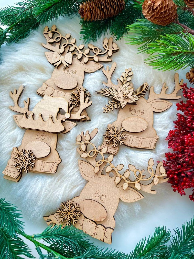May include: Four wooden reindeer ornaments with different decorations. Each reindeer has a brown wooden body with a white face and black eyes. The reindeer are decorated with snowflakes, greenery, and lights.