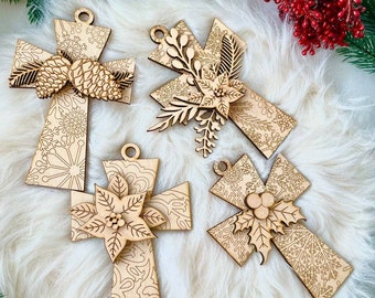 Puede incluir: Cuatro adornos navideños de madera en forma de cruces con intrincados diseños cortados con láser. Cada cruz presenta un motivo navideño diferente: una piña, una flor de pascua, bayas de acebo y un diseño floral.