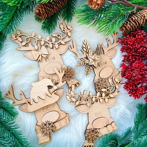 May include: Three wooden reindeer ornaments with different Christmas decorations. The reindeer are painted in a natural wood color and have white accents. The ornaments are surrounded by green pine branches and red berries.