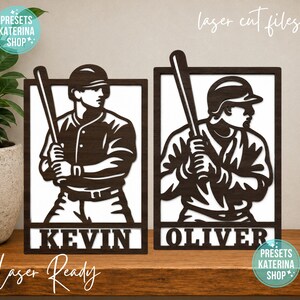May include: Two rectangular dark brown laser-cut wooden signs featuring baseball players holding bats. Each sign has a white background and displays a name at the bottom, with the left sign reading KEVIN and the right sign reading OLIVER.