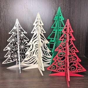 May include: Four wooden Christmas tree ornaments, one red, one green, and two white. The trees are all different designs and are made of laser-cut wood.