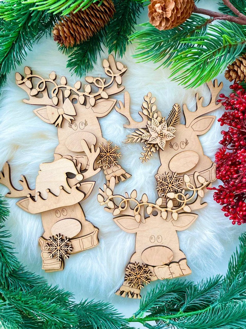 May include: Four wooden reindeer ornaments with different decorations. The reindeer are all facing forward with their antlers up. The ornaments are on a white fluffy background.