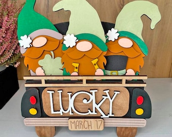 May include: Three gnomes in green hats and brown beards are riding in a black pickup truck. The truck has a wooden sign that says "LUCKY" and "MARCH 17".