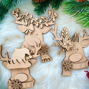 May include: Three wooden reindeer ornaments with different decorations. One reindeer has a bow, another has a snowflake and scarf, and the third has a poinsettia and holly.