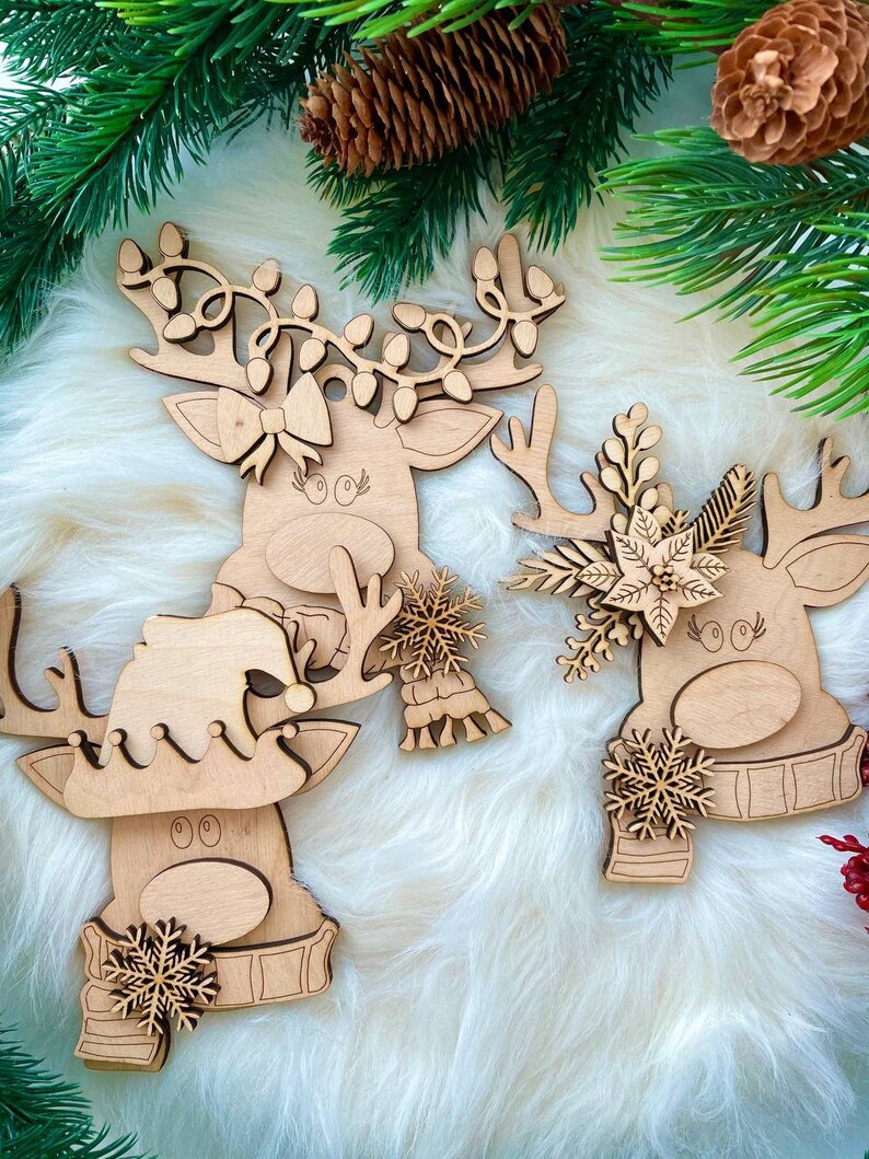 May include: Three wooden reindeer ornaments with different decorations. One reindeer has a bow, another has a snowflake and scarf, and the third has a poinsettia and holly.