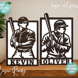 May include: Two rectangular dark brown laser-cut wooden signs featuring baseball players holding bats. Each sign has a white background and displays a name at the bottom, with the left sign reading KEVIN and the right sign reading OLIVER.
