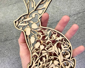 May include: A wooden cutout of a rabbit with intricate floral designs. The rabbit is standing on a base and is made of light brown wood.