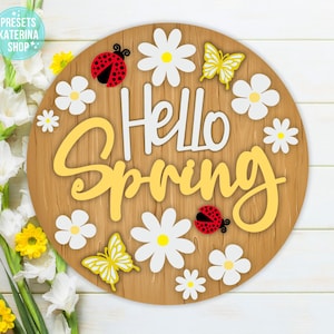 Könnte beinhalten: Ein rundes Holzschild mit dem Text "Hello Spring" in gelben Buchstaben. Das Schild ist mit weißen Gänseblümchen, roten Marienkäfern und gelben Schmetterlingen verziert.