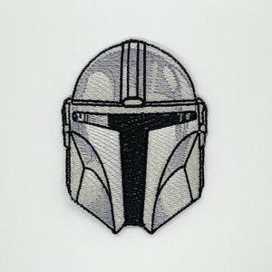 May include: A white and black embroidered patch of a Mandalorian helmet.