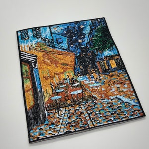 Puede incluir: Parche bordado con una representación vibrante de la pintura de Vincent van Gogh "La terraza de un café por la noche". El parche muestra una terraza de café con mesas y sillas bajo un cielo estrellado, con un edificio amarillo en el fondo.