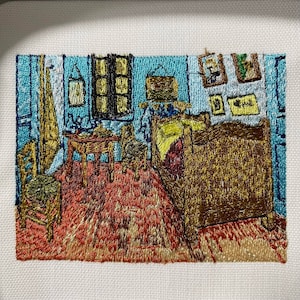 May include: Embroidered artwork depicting a bedroom interior with a wooden bed, a table with chairs, and a window. The walls are painted blue, and the floor is a red and orange patterned rug. There are several framed pictures on the wall.