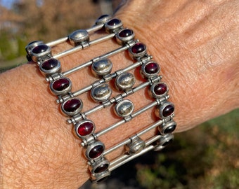 May include: A silver bracelet with a geometric design featuring alternating red gemstones and silver beads.