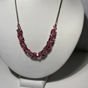 May include: A silver chain necklace with pink crystal beads. The necklace is on a white mannequin bust.