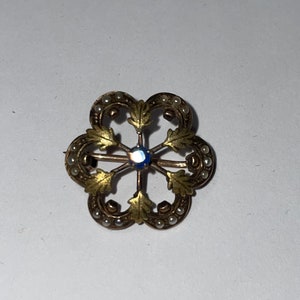 May include: A gold and pearl brooch with a blue center stone. The brooch is shaped like a flower with six petals.