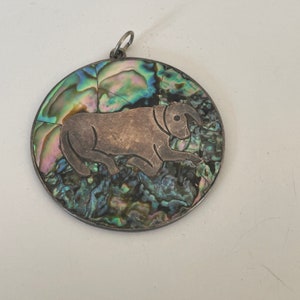 May include: A silver pendant with a bull design on a iridescent abalone shell background.