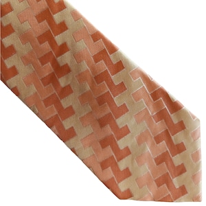 Puede incluir: Una corbata estampada con un diseño geométrico en tonos naranja y beige.