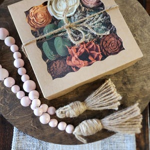 May include: A brown cardboard box with a clear window showcasing a variety of dried flowers and greenery. The flowers are in shades of pink, orange, and white, and the greenery is a deep green. The box is tied with twine and has a rustic, farmhouse aesthetic.
