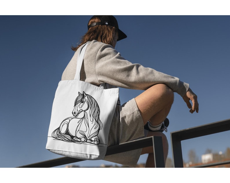 K&ouml;nnte beinhalten: Eine wei&szlig;e Einkaufstasche mit einer schwarzen Linienzeichnung eines Pferdes. Das Pferd liegt mit dem Kopf zur Seite gedreht. Die Tasche wird von einer Person getragen, die ein graues Sweatshirt und Shorts tr&auml;gt.
