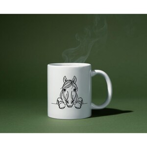 K&ouml;nnte beinhalten: Eine wei&szlig;e Keramiktasse mit einer schwarzen Linienzeichnung eines Pferdekopfes, der &uuml;ber den Rand schaut. Das Pferd hat eine lange M&auml;hne und eine gro&szlig;e Nase.