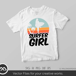 May include: White t-shirt with a retro sunset graphic featuring a silhouette of a surfer girl holding a surfboard. The text "SURFER GIRL" is printed in black below the graphic.