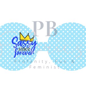 Könnte beinhalten: Eine blaue Brille mit weißen Punkten. Die linke Linse hat eine gelbe Krone und den Text "Sassy since forever" in Blau. Der Text "Profanity, Fun & Feminist" ist unter der Brille gedruckt.