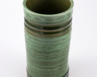 May include: A green ceramic vase with a textured surface and a brown rim. The vase has a wide opening and a cylindrical shape.