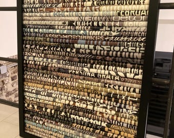 May include: A framed artwork made of rolled up pieces of paper with text printed on them. The paper is arranged in rows and is in shades of brown, black, and white. The text includes words like "The Good Life", "Heroes", "Motorbikes", and "Faussaire".