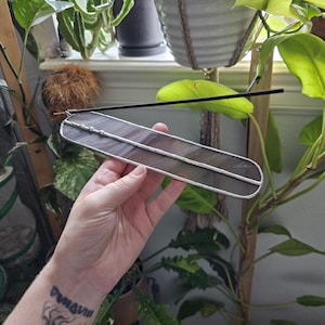 May include: A long, narrow, rectangular incense holder made of dark, semi-translucent purple stained glass with silver-toned metal solder edges. A single black incense stick is inserted into the small metal coil attached to one end.
