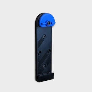 May include: A black phone mount with a blue swivel head. The mount has a textured surface and is designed to be attached to a wall.